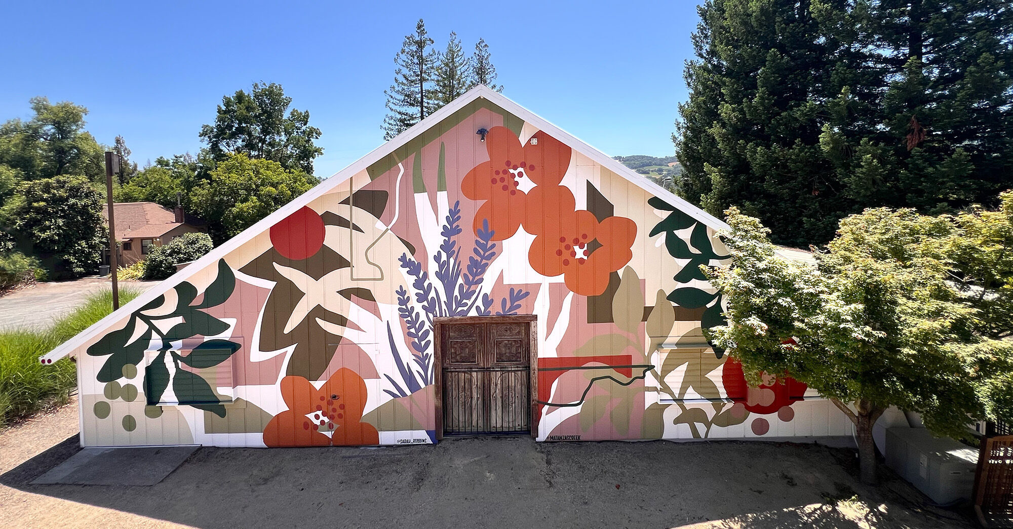 A colorful mural on a barn with a tree with greenery to the right of the frame.